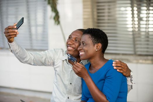 Portrait of two happy young people holding a credit card smiling and taking a picture on his smart phone