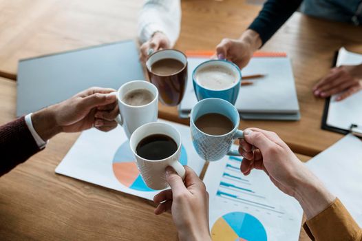 high angle people cheering with coffee mugs during office meeting. High resolution photo