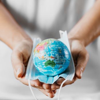 high angle person holding medical mask with earth globe. High resolution photo