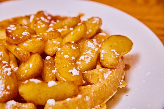 Image of Mouth-watering waffle covered in syrup apple slices and powdered sugar