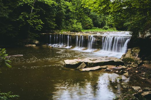 Image of Majestic falls over cliff edge in river surrounded by green forest