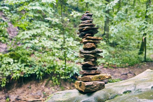 Image of Tall cairn stack of stones on muted green forest background
