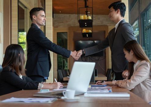 Group business people handshake at meeting table in office together with confident. Young businessman and businesswoman workers express agreement of investment deal.