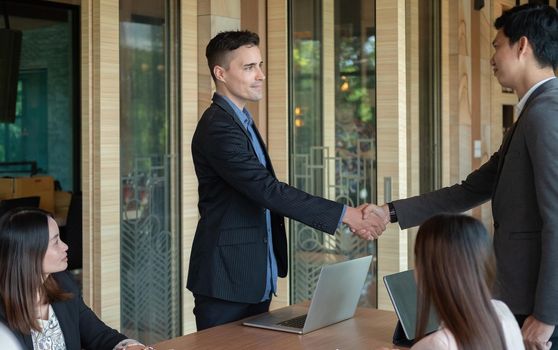 Group business people handshake at meeting table in office together with confident. Young businessman and businesswoman workers express agreement of investment deal.