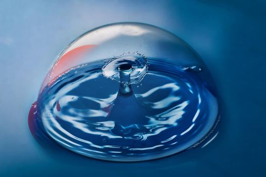 Image of Blue surface with clean bubble containing ripples from two water drops colliding in air