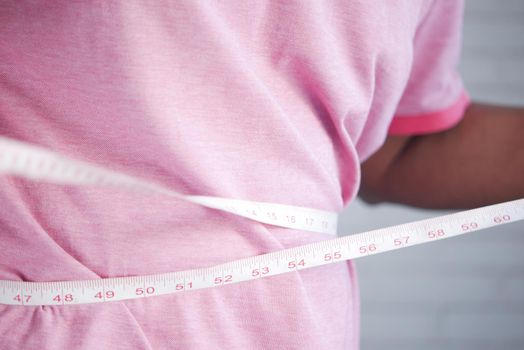 young man measuring his waist with a tape measure, close up