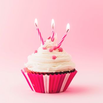 fresh birthday cupcake with burning candles pink backdrop. Beautiful photo