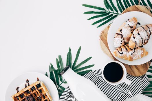 overhead view baked croissant waffles bottle coffee cup leaves white backdrop. Beautiful photo