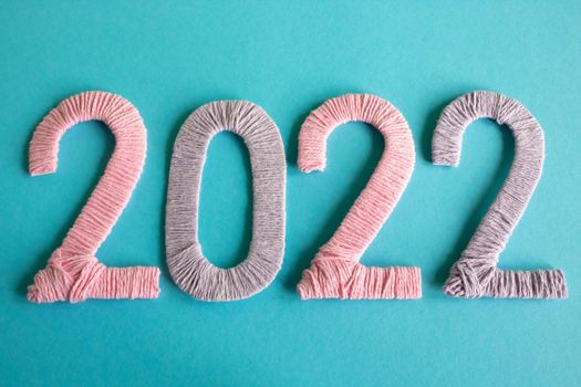 Knitted figures 2022, made of pink and lilac threads, lie on a blue background. The concept of the New Year.