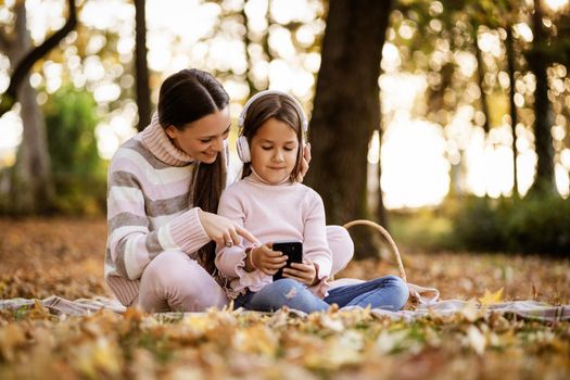 Mother and daughter enjoying autumn in park. Little girl is learning to read.