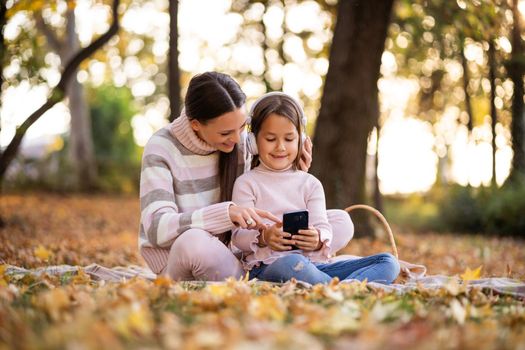 Mother and daughter enjoying autumn in park. Little girl is learning to read.