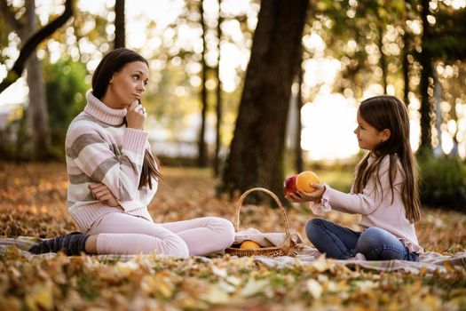 Mother and daughter having picnic in park in autumn.