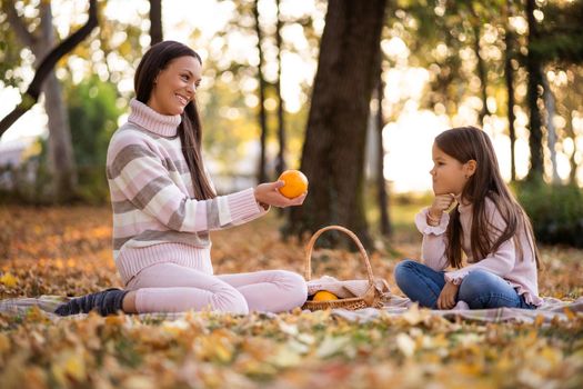 Mother and daughter having picnic in park in autumn.