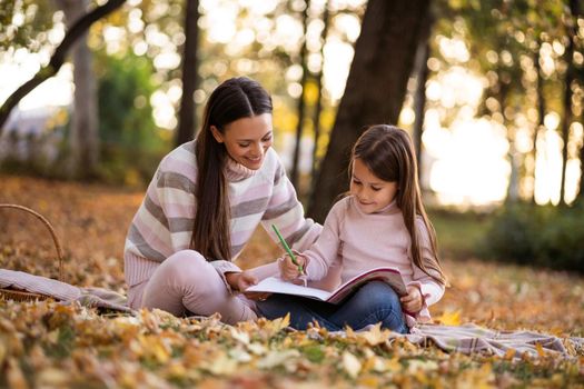 Mother and daughter enjoying autumn in park. Little girl is drawing.