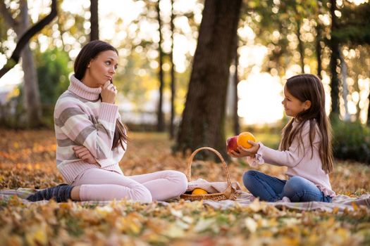 Mother and daughter having picnic in park in autumn.