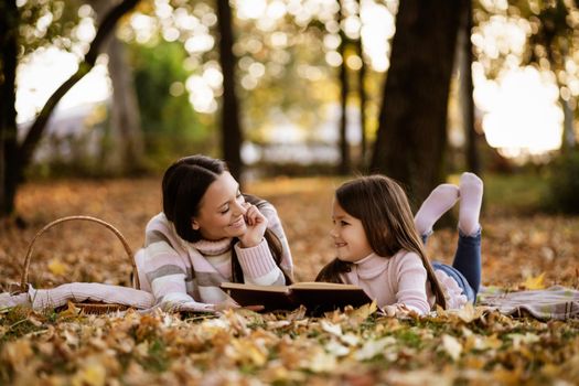 Mother and daughter enjoying autumn in park. Little girl is learning to read.