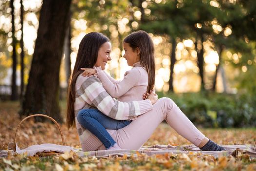 Mother and daughter enjoying autumn in park. They are embracing.