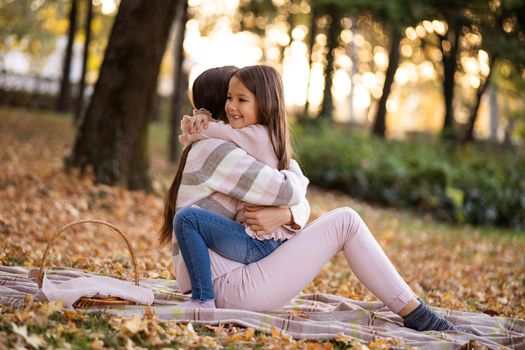 Mother and daughter enjoying autumn in park. They are embracing.