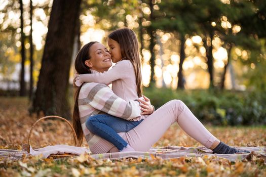 Daughter is kissing her mother in autumn in park.