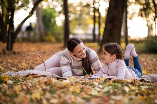 Mother and daughter enjoying autumn in park. Little girl is drawing.