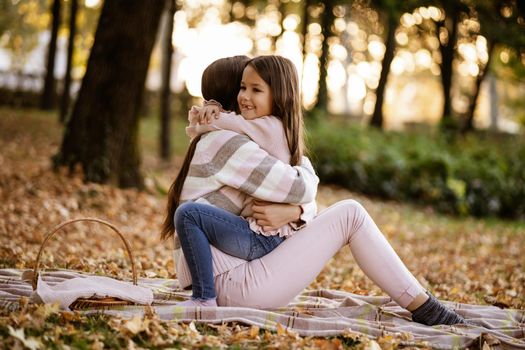 Mother and daughter enjoying autumn in park. They are embracing.