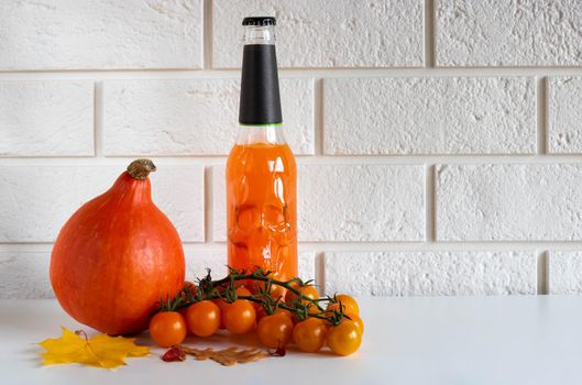 A bottle of orange drink with a skull, ripe pumpkin vegetables and orange cherry tomatoes on a white background.Halloween concept. Place for your text.