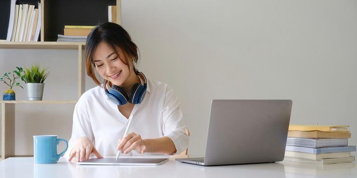 Young undergraduate student studying online class by laptop computer and taking note on digital tablet