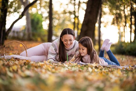 Mother and daughter enjoying autumn in park. Little girl is learning to read.