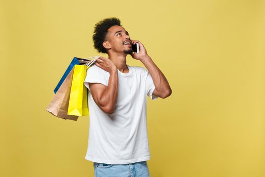 young man with shopping bags talking on smart phone isolated on yellow background.