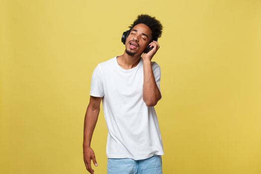 Close up portrait of dark skinned man with closed eyes, has headphones, listens to favourite music. Teenager enjoys audio track isolated on yellow background