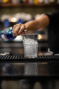 woman's hand pouring blue liqueur into a glass with ice