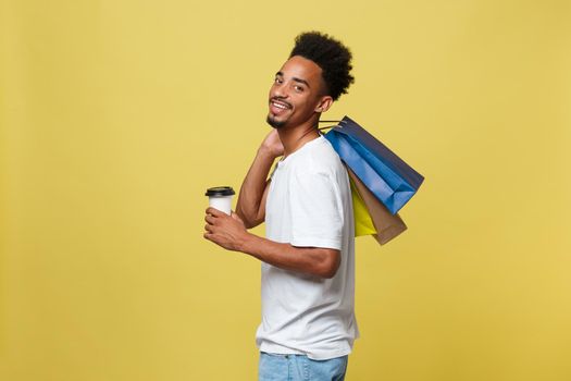 African American man with colorful paper bags isolated on yellow background.