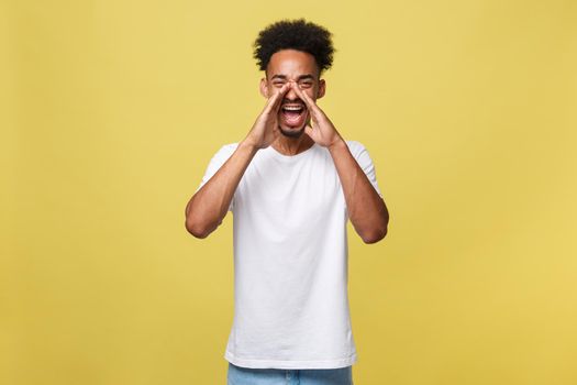 positive young black guy, student, worker employee screams mouth wide open and putting his hands to his face as mouthpiece. Portrait on white background in casual clothing