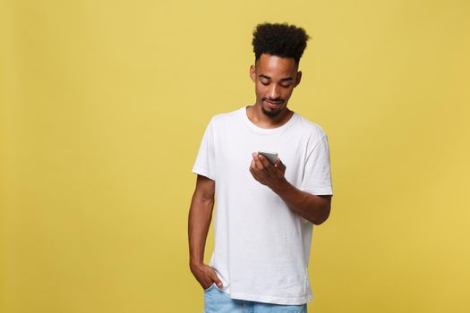 Happy african american man with smiling and using mobile phone. Isolated on yellow background