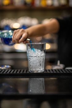 woman's hand pouring blue liqueur into a glass with ice