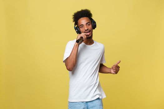 Attractive young dark-skinned man with afro haircut in white t shirt, gesticulating with hands and microphone, dancing and singing on party, having fun