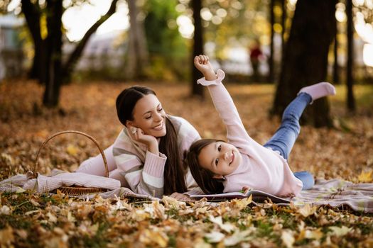 Mother and daughter enjoying autumn in park. Little girl is drawing.