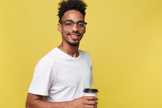 Stylish young afro american man holding cup of take away coffee isolated over yellow background.