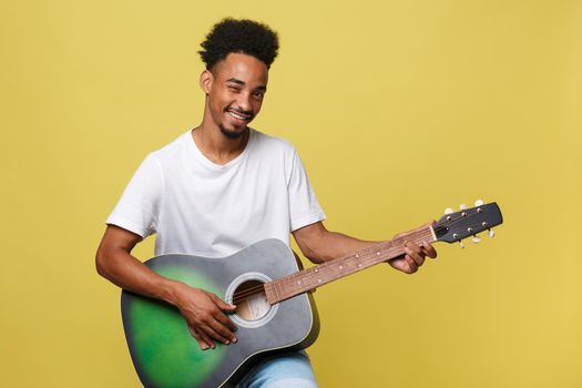 Happy african american musician man posing with a guitar, over golden yellow background