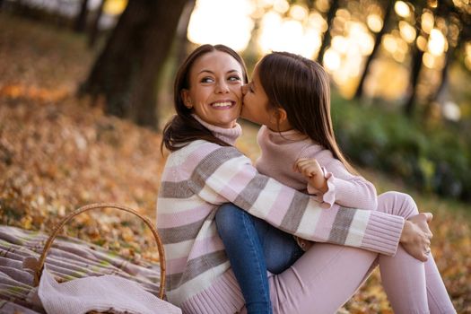 Daughter is kissing her mother in autumn in park.