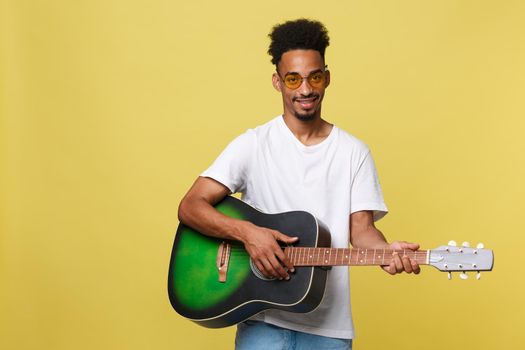 Happy african american musician man posing with a guitar, over golden yellow background