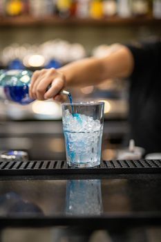 woman's hand pouring blue liqueur into a glass with ice