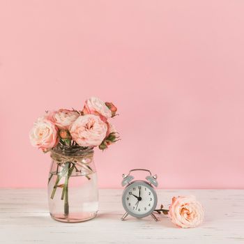 roses vase near alarm clock wooden desk against pink background. High resolution photo