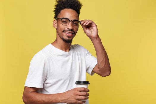 Stylish young afro american man holding cup of take away coffee isolated over yellow background.