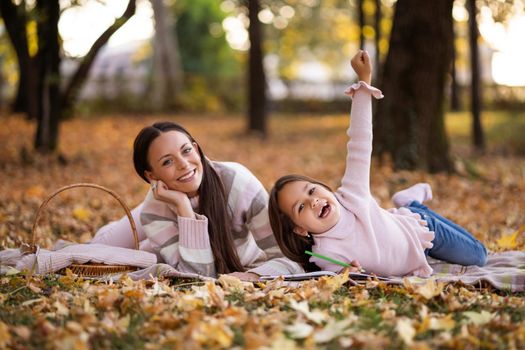 Mother and daughter enjoying autumn in park. Little girl is drawing.