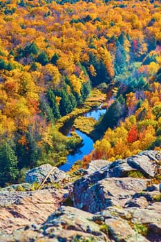 Image of Winding river that disappears under a rocky outcropping and surrounded by a forest in fall