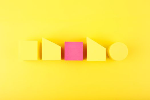 Yellow minimal abstract composition with yellow and pink geometric shapes in a row against yellow background. Individuality and being different concept. 