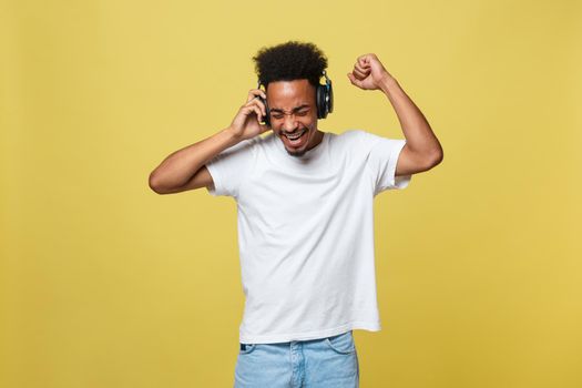 Young African American man wearing headphone and enjoy music over yellow gold Background.