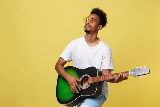 Happy african american musician man posing with a guitar, over golden yellow background