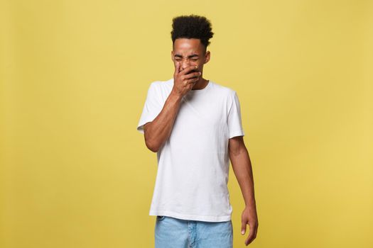 Portrait of attractive sleepy african-american male model in trendy black hat, yawning, covering mouth with palm and stretching, feeling tired and sleepy over yellow background.